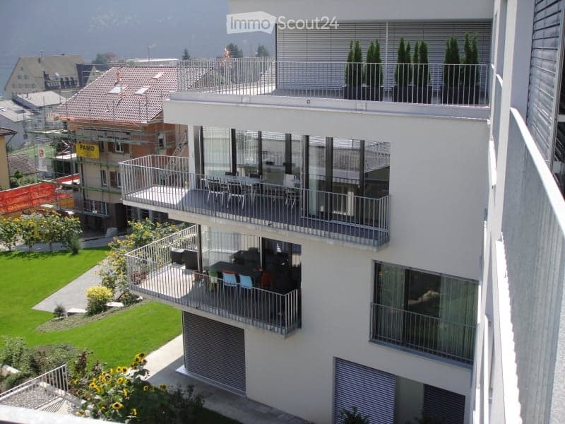 Modern multi-story building with multiple balconies, outdoor seating, and a scenic view of the surrounding area.
