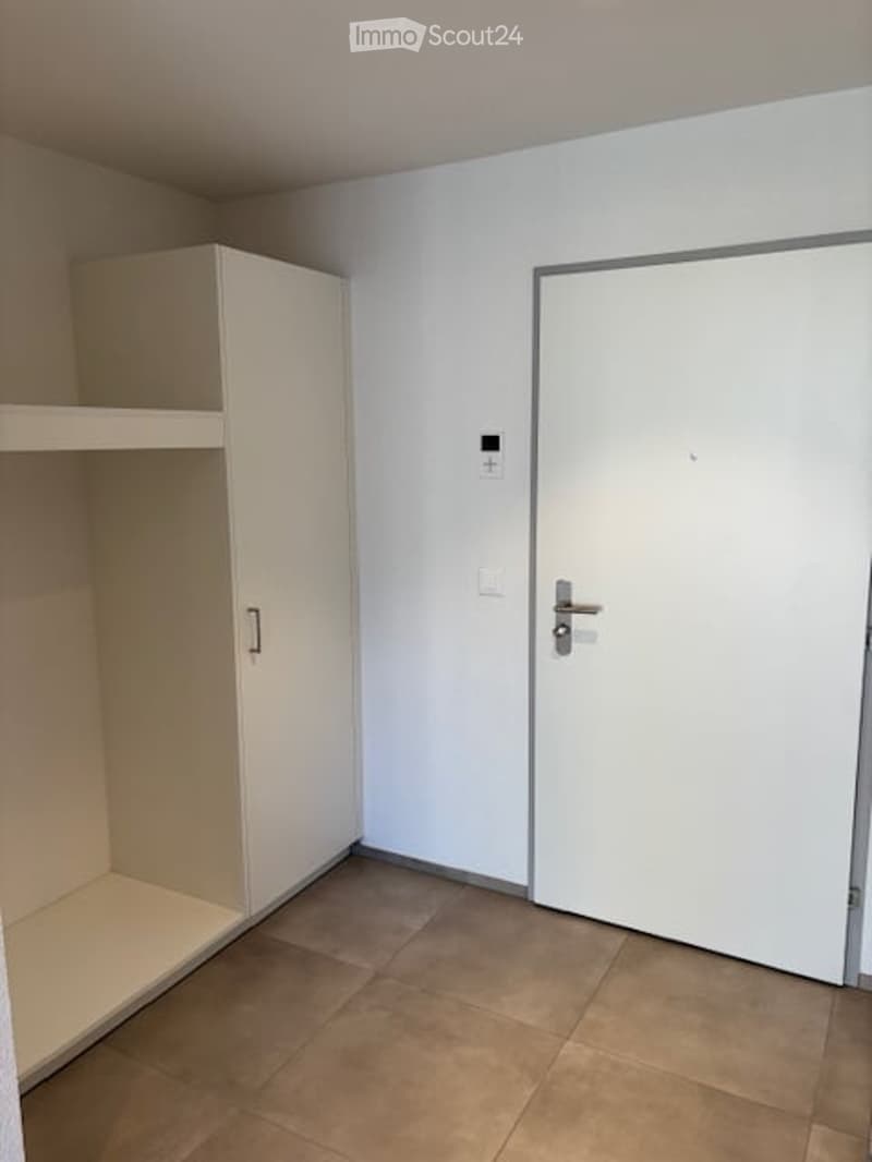 Empty room with light-colored walls, tiled floor, white cabinet, and a closed white door.