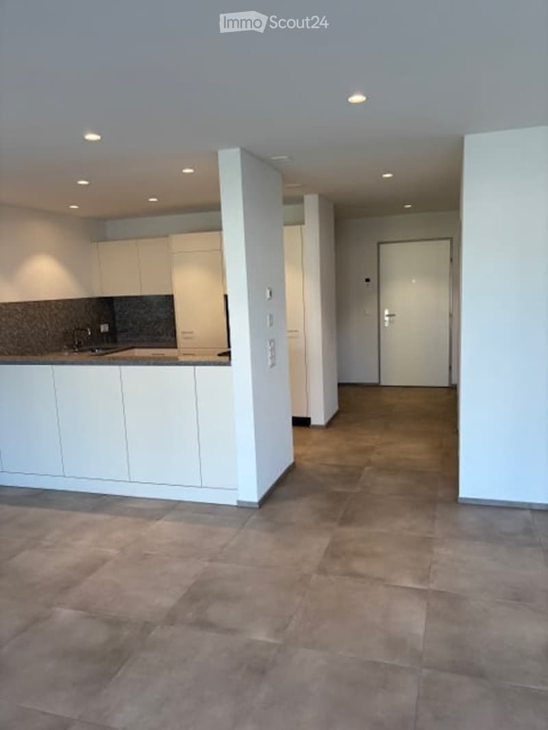 Open-plan kitchen and living area with white cabinetry, tiled floor, and recessed lighting. No furniture or personal items present.