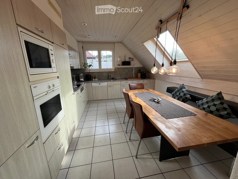 Modern kitchen and dining area with light wood cabinets, stainless steel appliances, a large wooden dining table, and pendant lights.