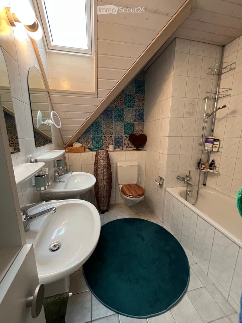 Modern bathroom with two sinks, a toilet, a bathtub, a shower, and a decorative vase. The walls are tiled with a mix of white and blue tiles, and there is a large mirror above the sinks.