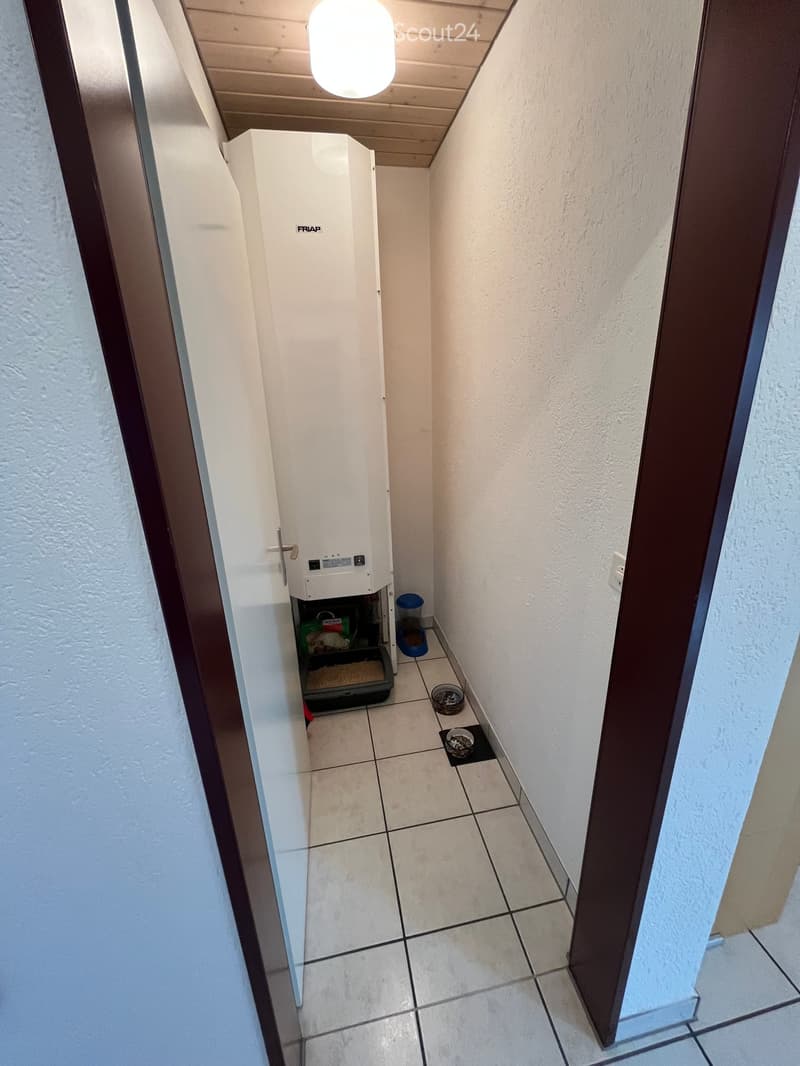 Narrow hallway with tiled floor, white walls, and a pet feeding station including a water dispenser, food container, and litter box.