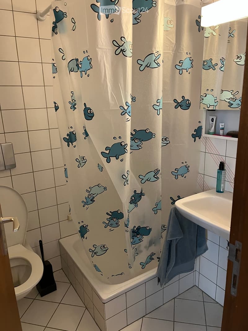 Bathroom with a bathtub, toilet, sink, and a shower curtain featuring fish designs. A towel is draped over the edge of the sink, and a bottle is placed on the shelf above the sink.