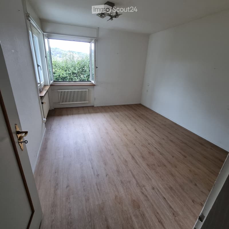 Empty room with wooden flooring, white walls, large windows, radiator, and a door with a golden handle.