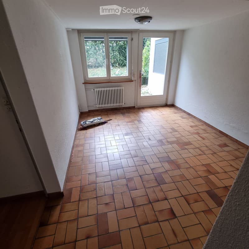 Empty room with tiled floor, white walls, large windows, and a radiator. No furniture or equipment present.