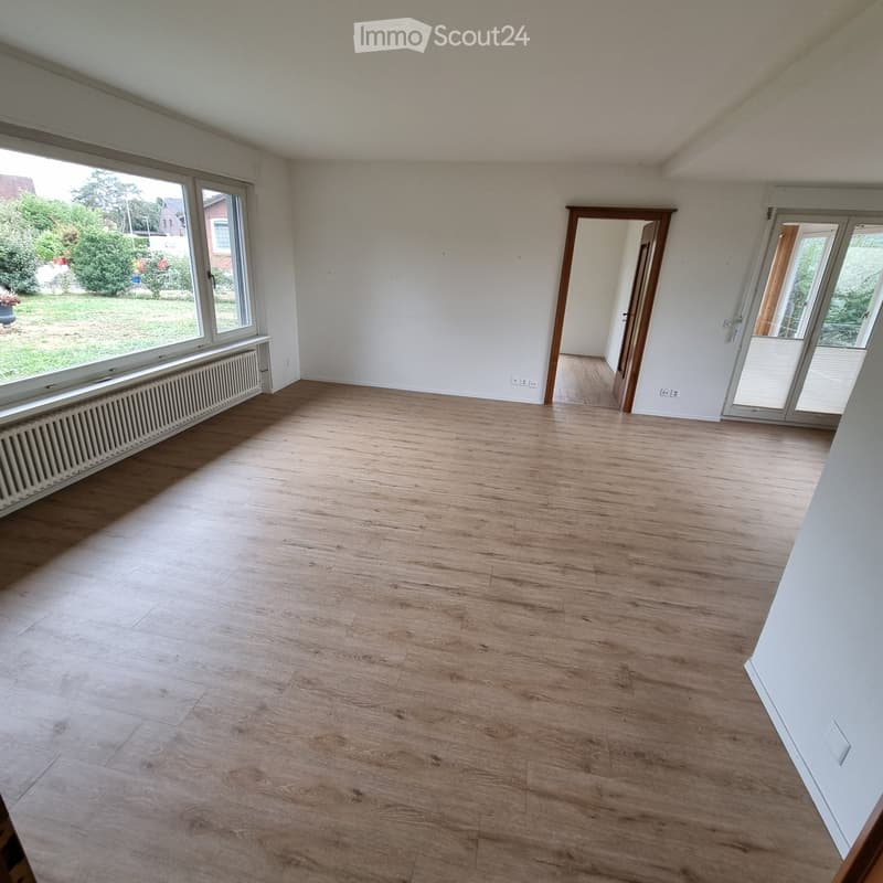 Empty room with wooden flooring, large windows, and a sliding glass door leading to an outdoor area.