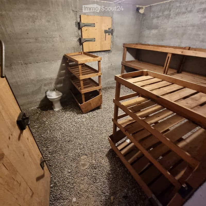 Bathroom with concrete walls, gravel floor, toilet, and wooden shelves.