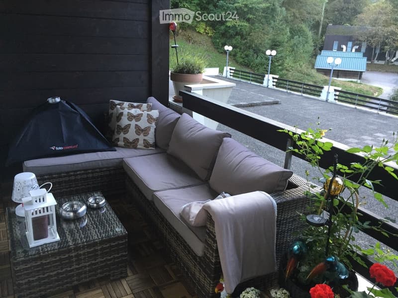 Balcony with a wicker sofa, throw pillows, a small table with a lantern, and potted plants.