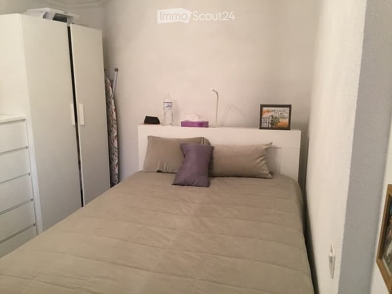 A small, neatly arranged bedroom with a single bed, pillows, a wardrobe, a lamp, and a picture frame on the headboard.