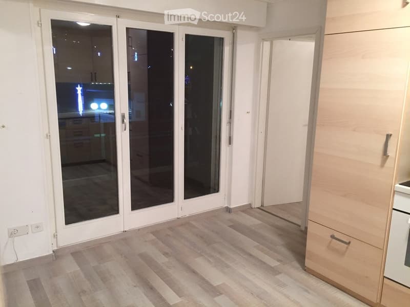 Empty room with wooden flooring, white walls, and large glass sliding doors leading to another space.
