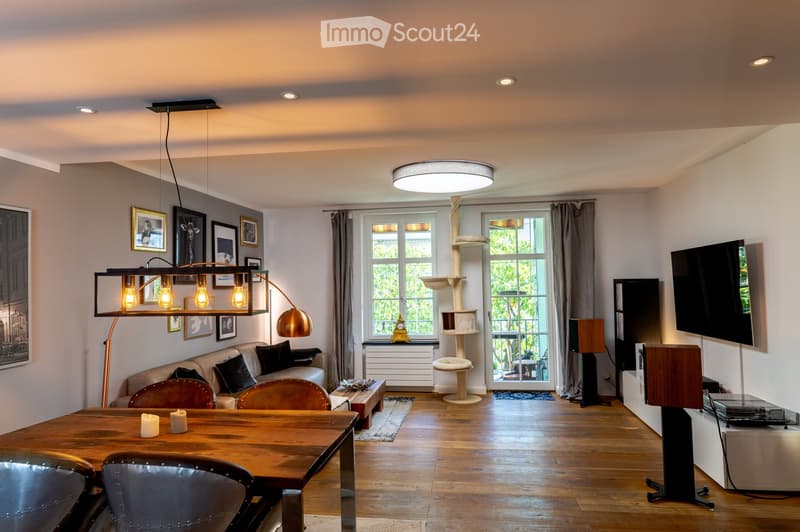 Bright living room with wooden flooring, large windows, a cat tree, a sofa, a dining table, and a television.