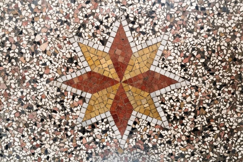 Close-up of a mosaic tile floor with intricate geometric patterns in red, yellow, and white tiles.