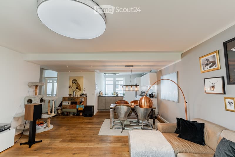 Open-plan living and dining area with wooden flooring, a modern sofa, a dining table with chairs, a cat tree, and decorative artwork on the walls.