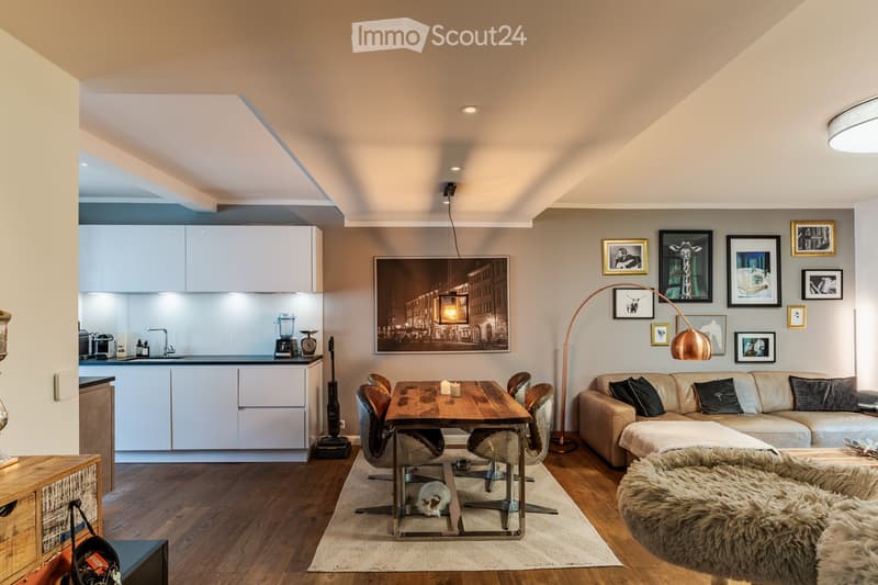 Modern open-plan living and dining area with a sofa, dining table, chairs, kitchen area, and artwork on the walls.