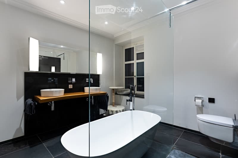 Modern bathroom with a freestanding bathtub, double sink vanity, toilet, large mirror, and a glass-enclosed shower area.