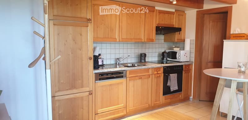 A cozy kitchen with wooden cabinets, a stainless steel sink, a microwave, an oven, and a small round table with a glass on it.