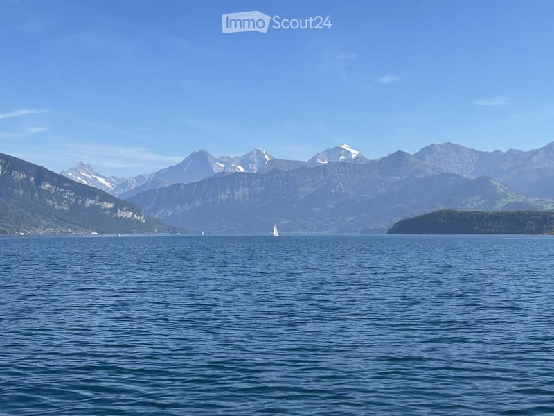 A serene lake view with snow-capped mountains in the background and a sailboat on the water.