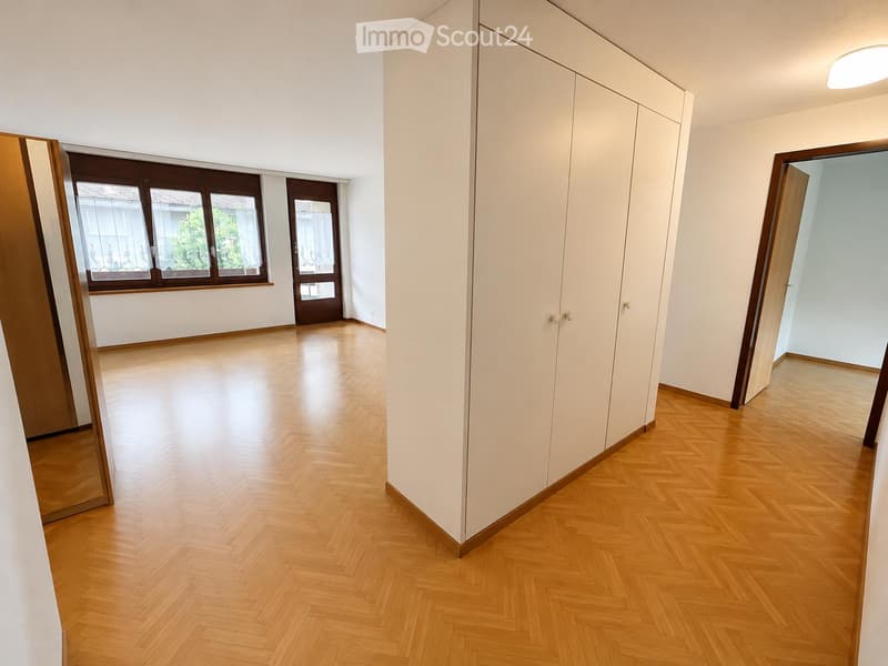 Empty room with wooden flooring, white walls, large window with curtains, and a tall white wardrobe. No furniture or personal items present.
