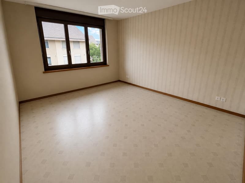 Empty room with beige tiled floor, light-colored walls, and a large window with wooden frame. No furniture or equipment present.