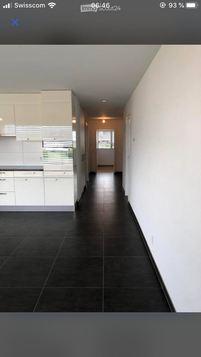Empty hallway with dark tiled flooring, white walls, and a view into a modern kitchen area with white cabinets and stainless steel appliances.