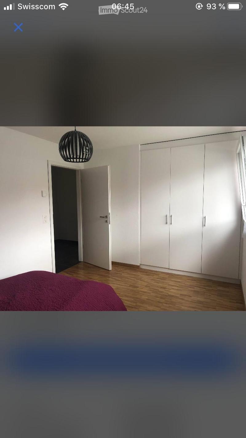 A modern bedroom with a wooden floor, a red bedspread, a large white wardrobe, and a stylish black pendant light.