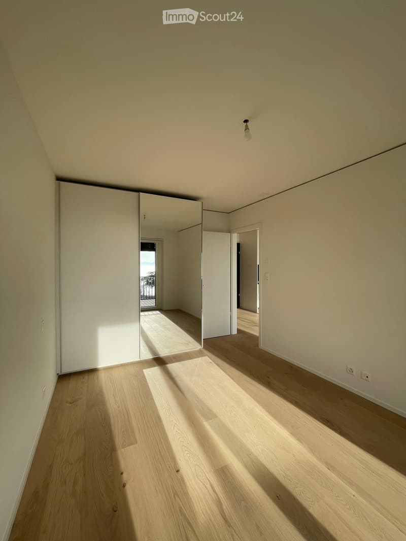 Empty hallway with light wooden flooring, white walls, and a sliding door leading to a balcony area.