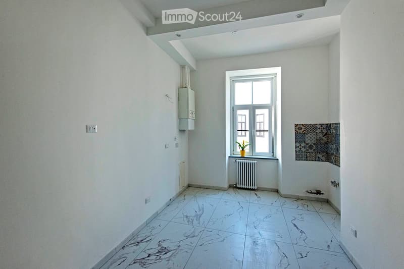 Empty room with white walls, marble tiled floor, a window with a small plant on the sill, radiator, and electrical outlets.