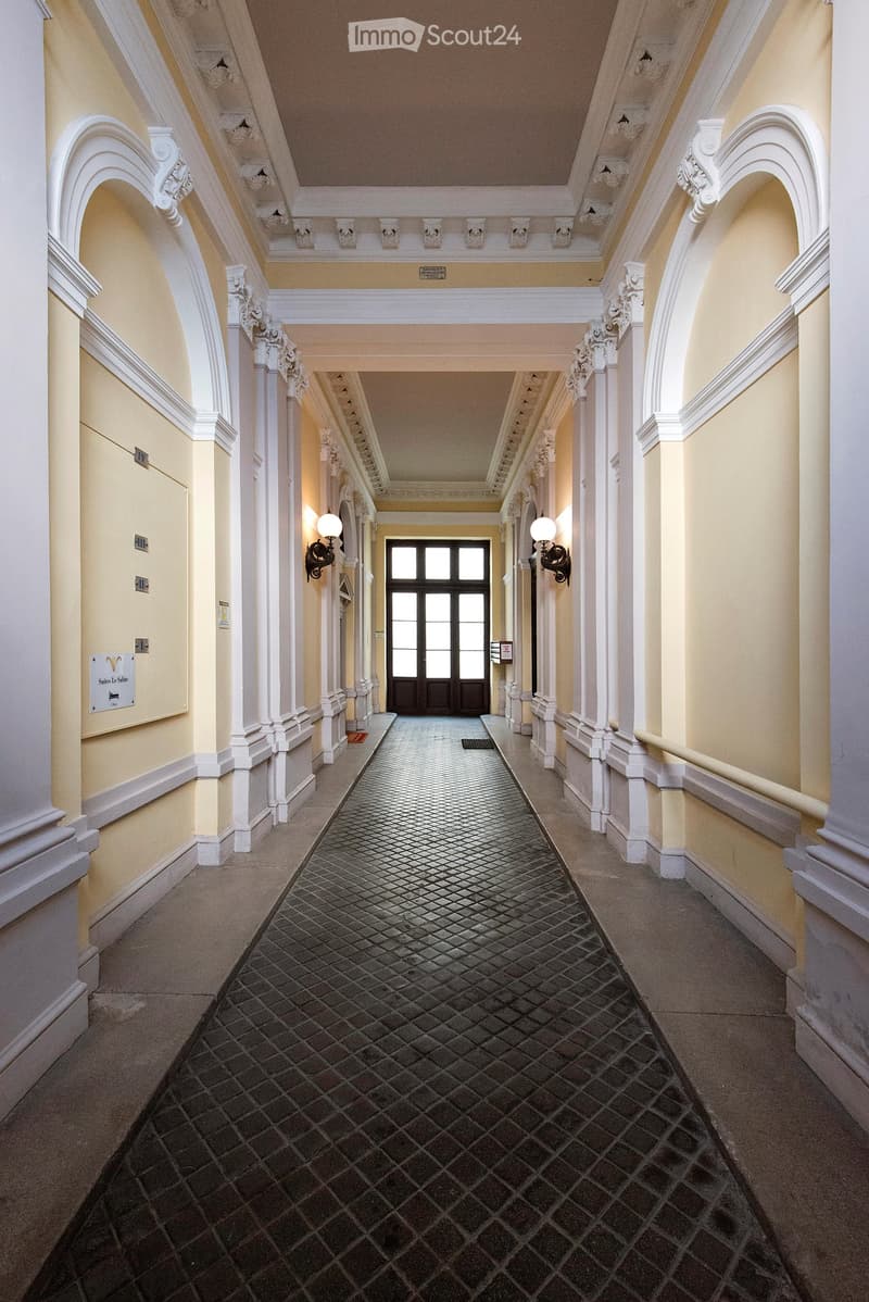 Elegant hallway with a patterned tile floor, white columns, arched doorways, and decorative wall sconces.