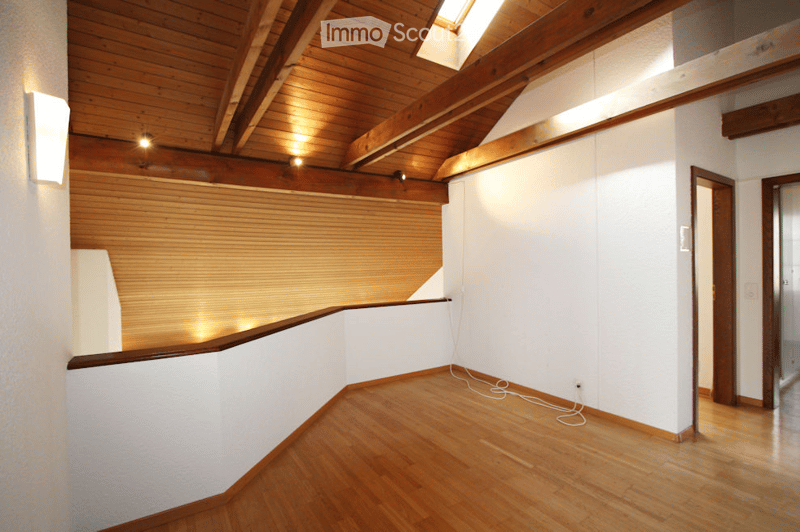 Empty room with wooden floor, white walls, exposed wooden ceiling beams, and a skylight window. No furniture or equipment present.