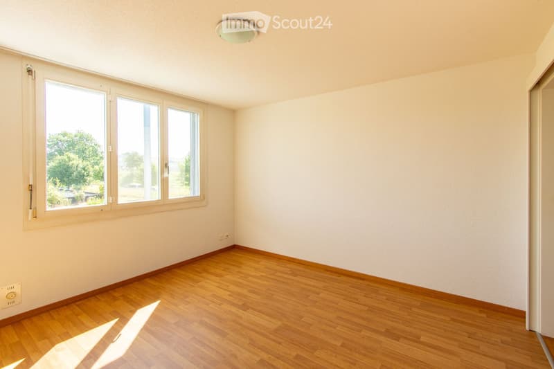 Empty room with wooden flooring, white walls, and large windows letting in natural light. No furniture or equipment present.