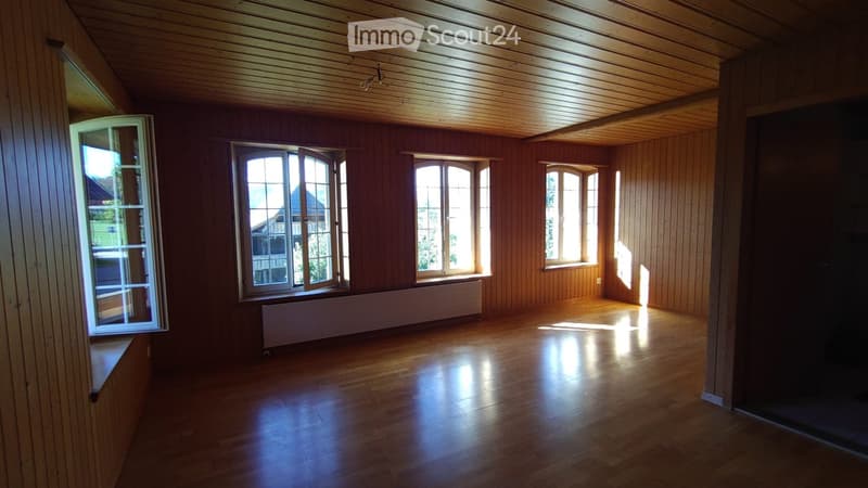 Empty room with wooden walls, wooden ceiling, and wooden floor, featuring multiple windows and a radiator under one window.