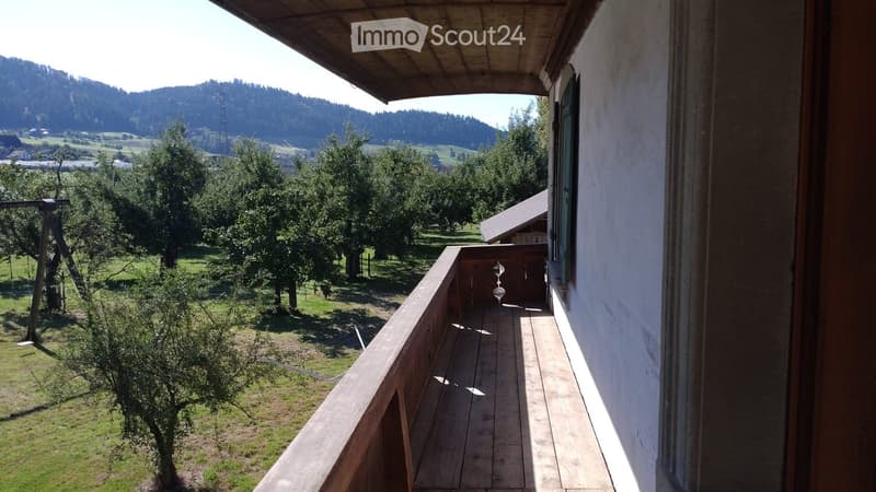 Wooden balcony with a view of a green landscape, trees, and distant hills.