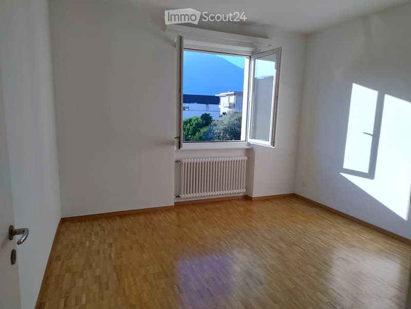 Empty room with wooden wall paneling, white walls, and a window with blinds, allowing natural light to enter.