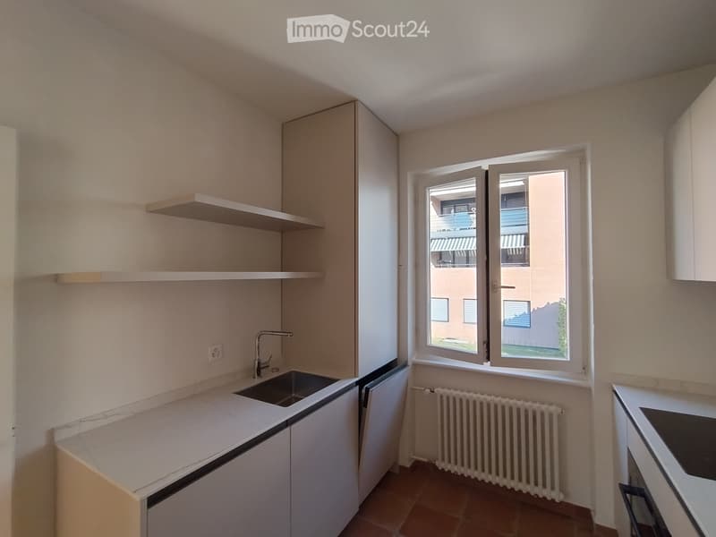 Empty room with white walls, a window, radiator, and built-in cabinets.