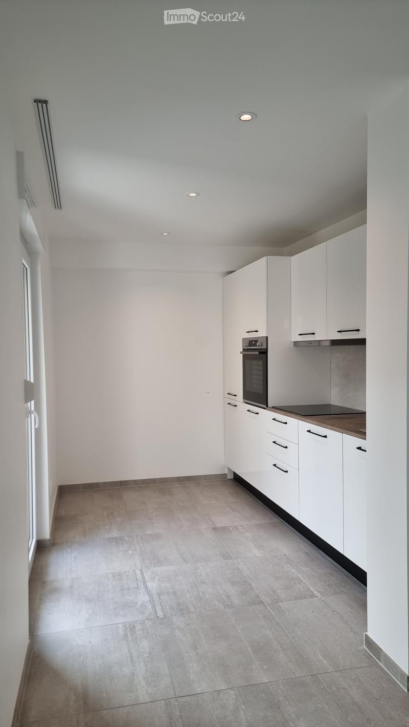 Empty kitchen with white cabinets, a countertop, and a built-in oven. The space features a tiled floor and recessed ceiling lighting.