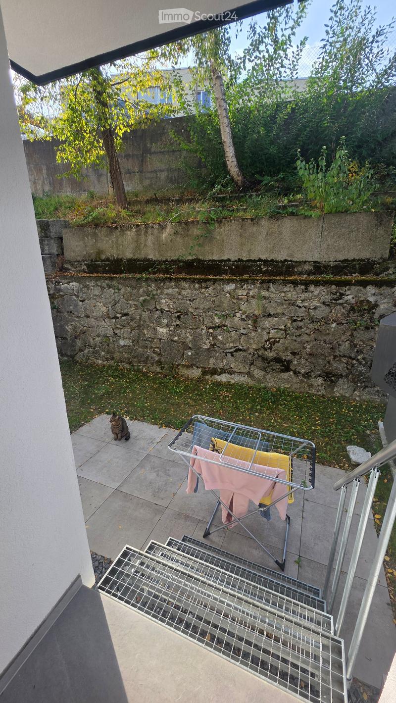 Balcony with tiled floor, metal railing, laundry rack with clothes, and a cat sitting nearby.