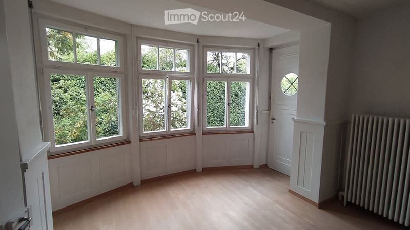 Empty room with wooden flooring, large windows, white walls, and a radiator. No furniture or equipment present.