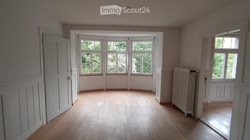 Empty room with wooden flooring, large windows, white walls, and a radiator. No furniture or equipment present.
