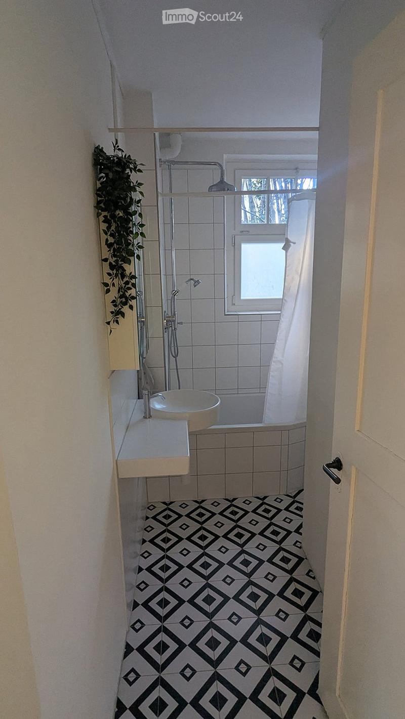 Modern bathroom with a black and white geometric tile floor, a white sink with a chrome faucet, a glass-enclosed shower, and a small window with a view of greenery.