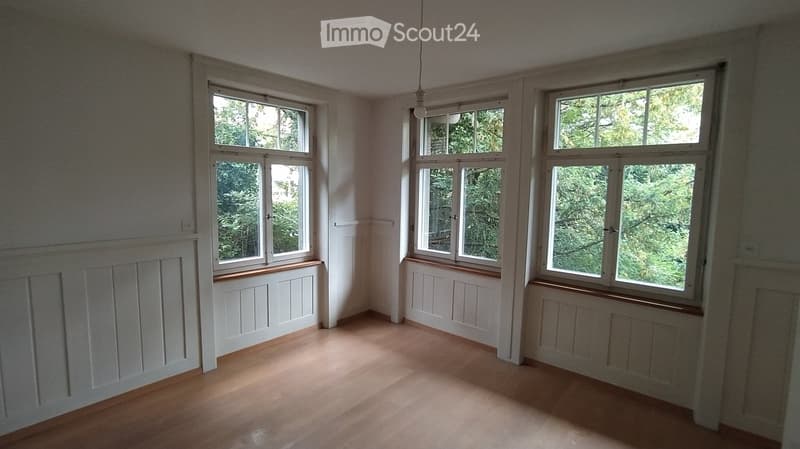 Empty room with wooden flooring, white walls, and large windows with wooden sills. No furniture or equipment present.