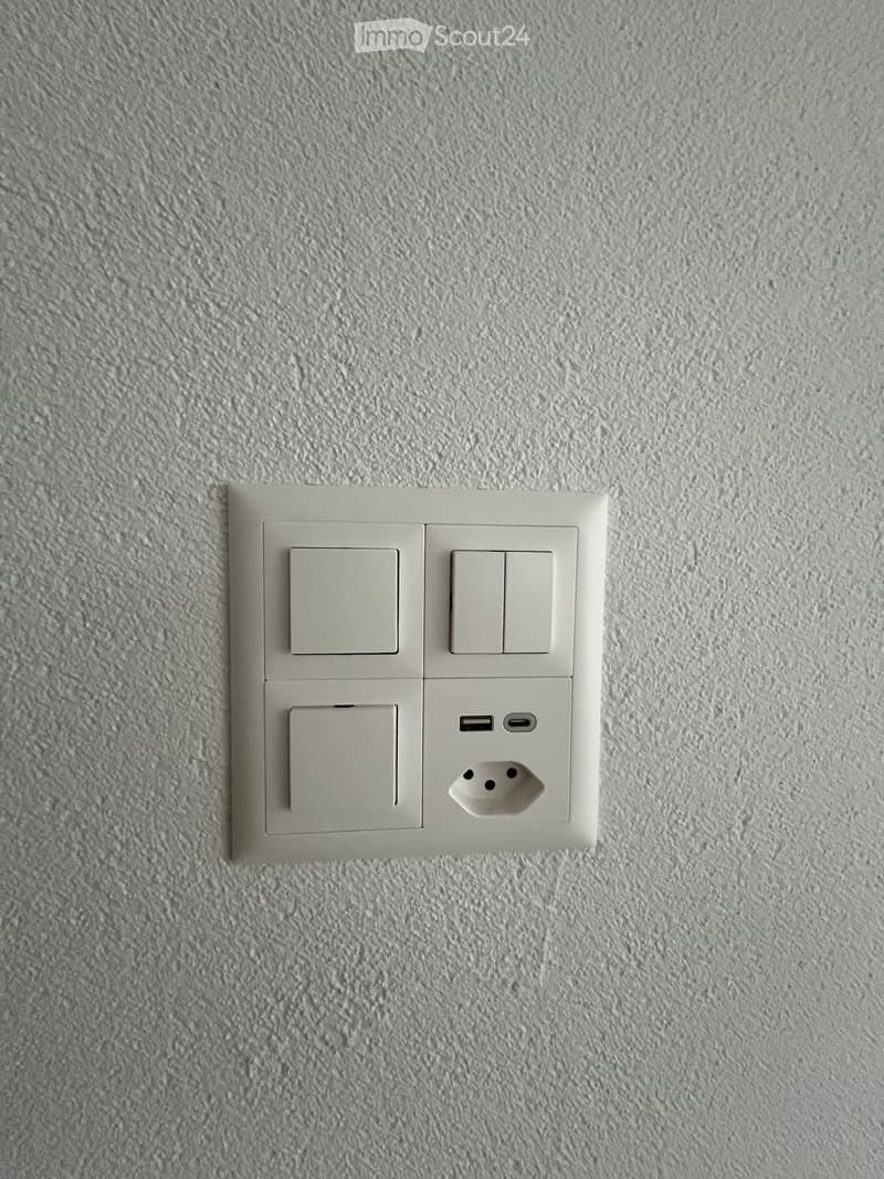 A modern wall-mounted electrical outlet with multiple USB ports and standard sockets, mounted on a textured grey wall.