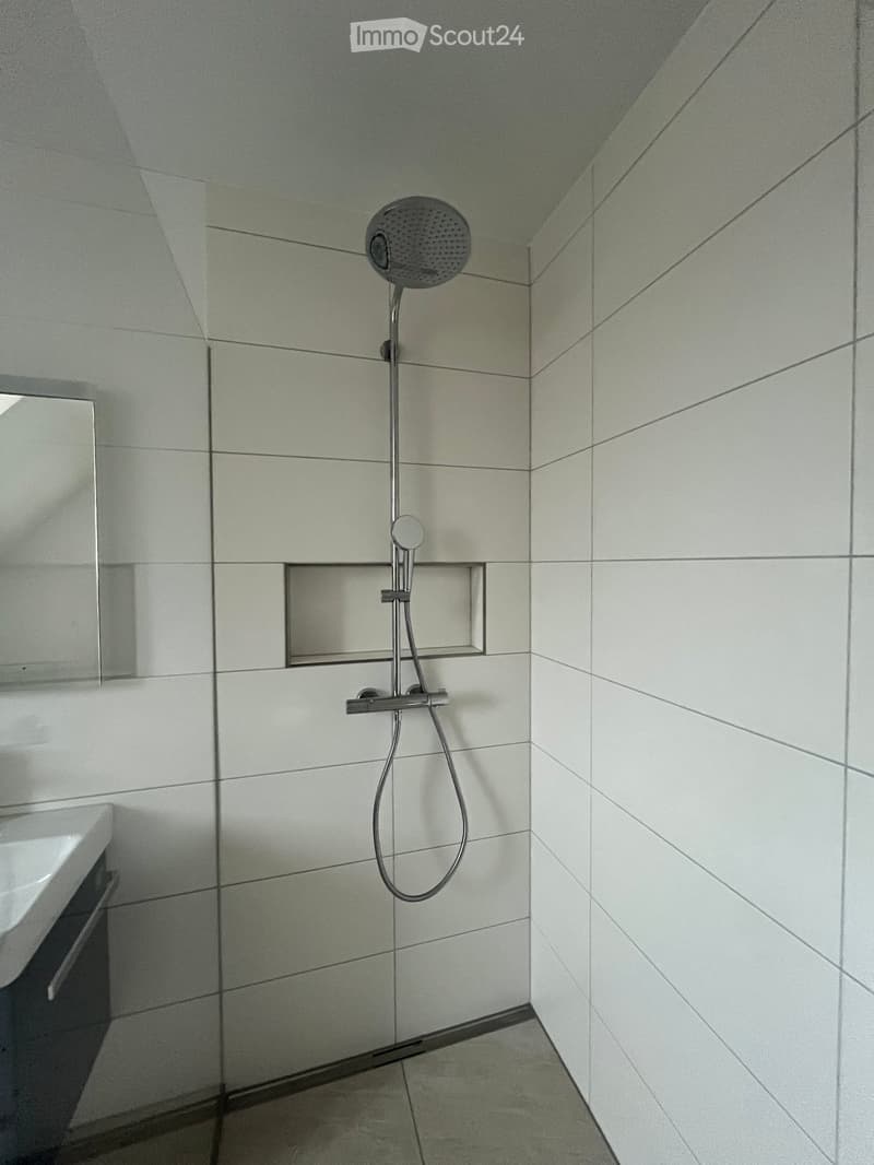 Modern bathroom with white tiled walls and floor, featuring a handheld showerhead and a built-in shelf.