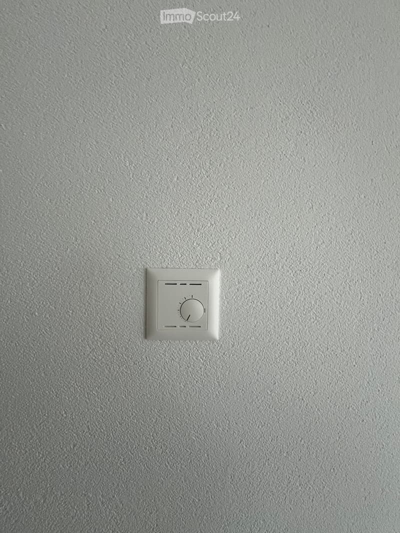 A modern light switch with a dial and two buttons mounted on a textured gray wall.
