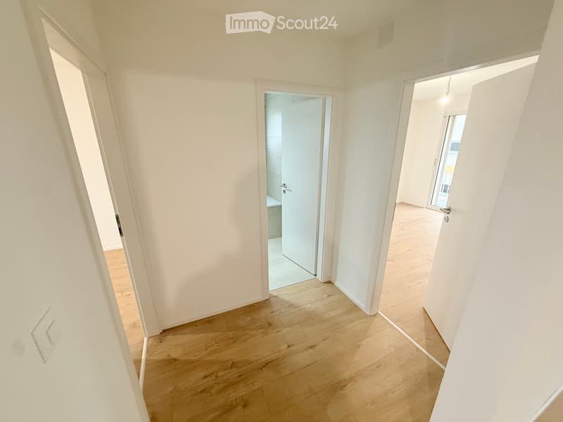 Empty hallway with light wooden flooring and white walls, featuring several open doors leading to other rooms.