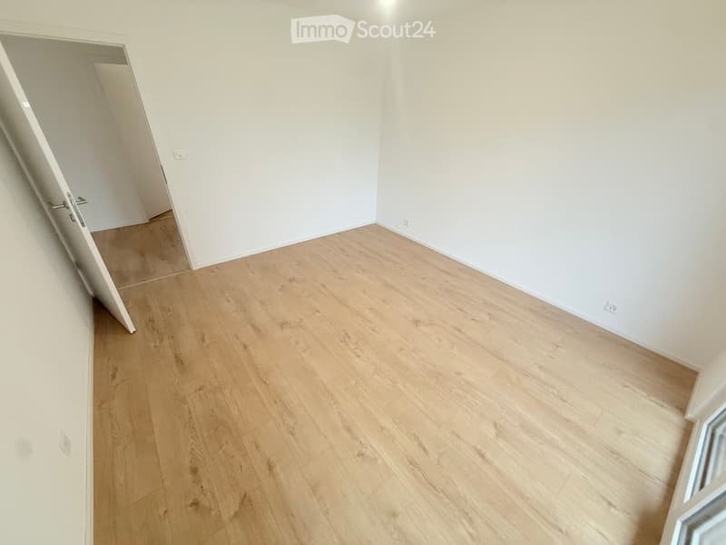 Empty room with light wooden flooring and white walls, featuring an open doorway leading to another space.