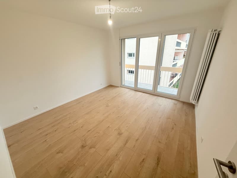 Empty room with light wooden flooring, white walls, and large sliding glass doors leading to a balcony.