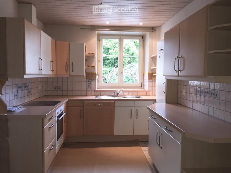 Bright kitchen with white cabinets, a sink, and an oven, featuring a window with a view of greenery.