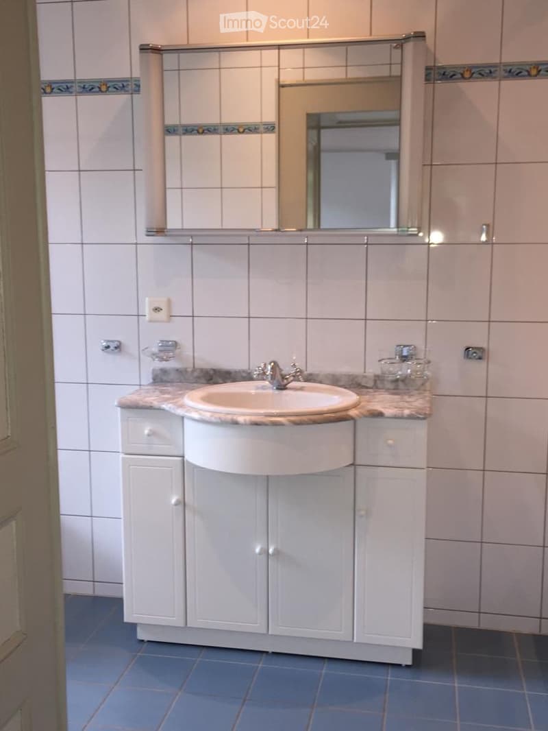 Bathroom with white tiled walls, a white sink with a chrome faucet, a large mirror above, and white cabinets with marble countertop.