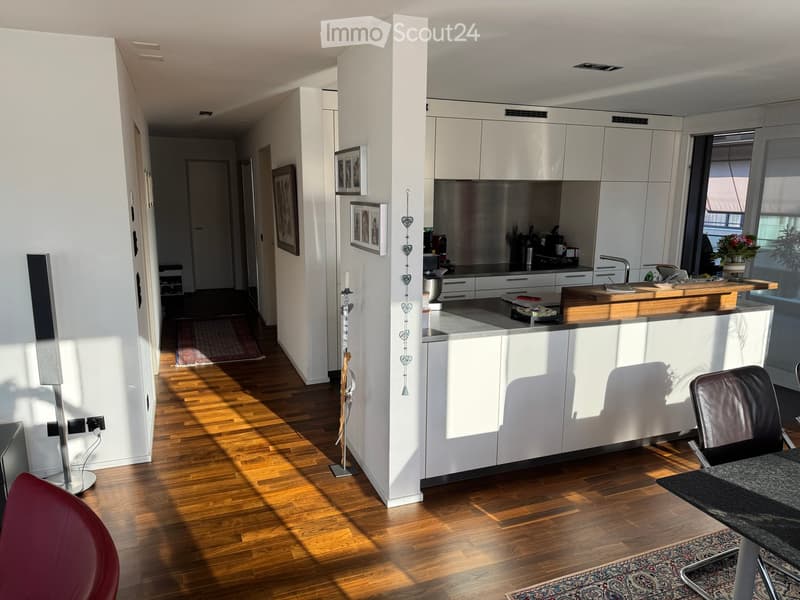 Modern kitchen with white cabinets, a central island, and a dining area. Features include a wooden countertop, a sink with a faucet, a chair, a table, and a speaker on the floor.