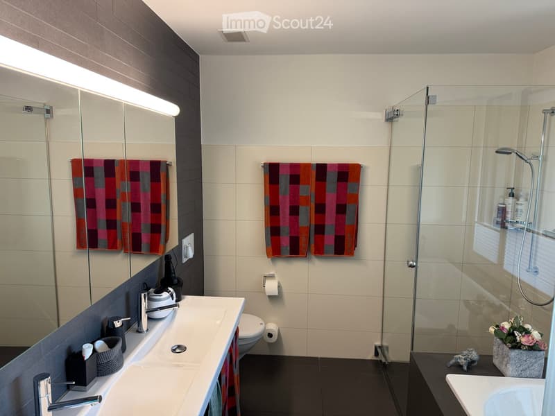 Modern bathroom with double sink, large mirror, glass shower enclosure, and decorative towels.